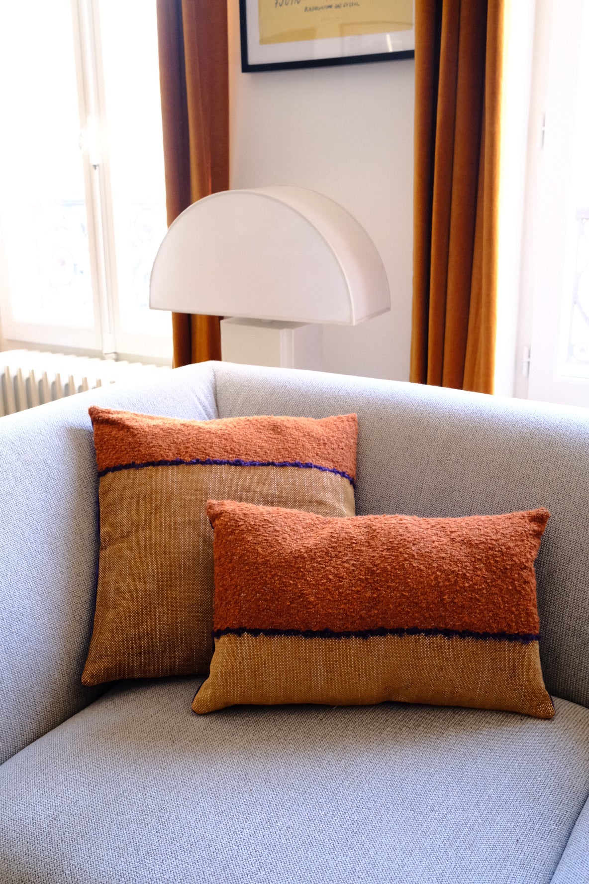 Coussin Horizon, 30x50cm. Les tons camel se marient merveilleusement au velours violet et lumineux de son verso. Les tissus viennent de la maison Elitis. Le coussin a été cousu à la main à Paris par l'un de nos artisans. Ici sur un canapé gris clair.