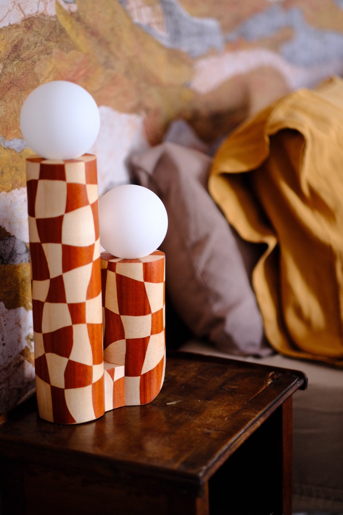 Lampe en marqueterie de bois et sa robe à carreaux pour Ome éditions. Damier en bois de padouk (bois rouge) et Sycomore (bois blanc). Pièce fabriquée à la main par Hermine Torikian, notre artiste ébéniste. Son atelier est à Paris. Lampe à poser sur une étagère, un table de chevet, dans une bibliothèque... Ici sur une table de nuit