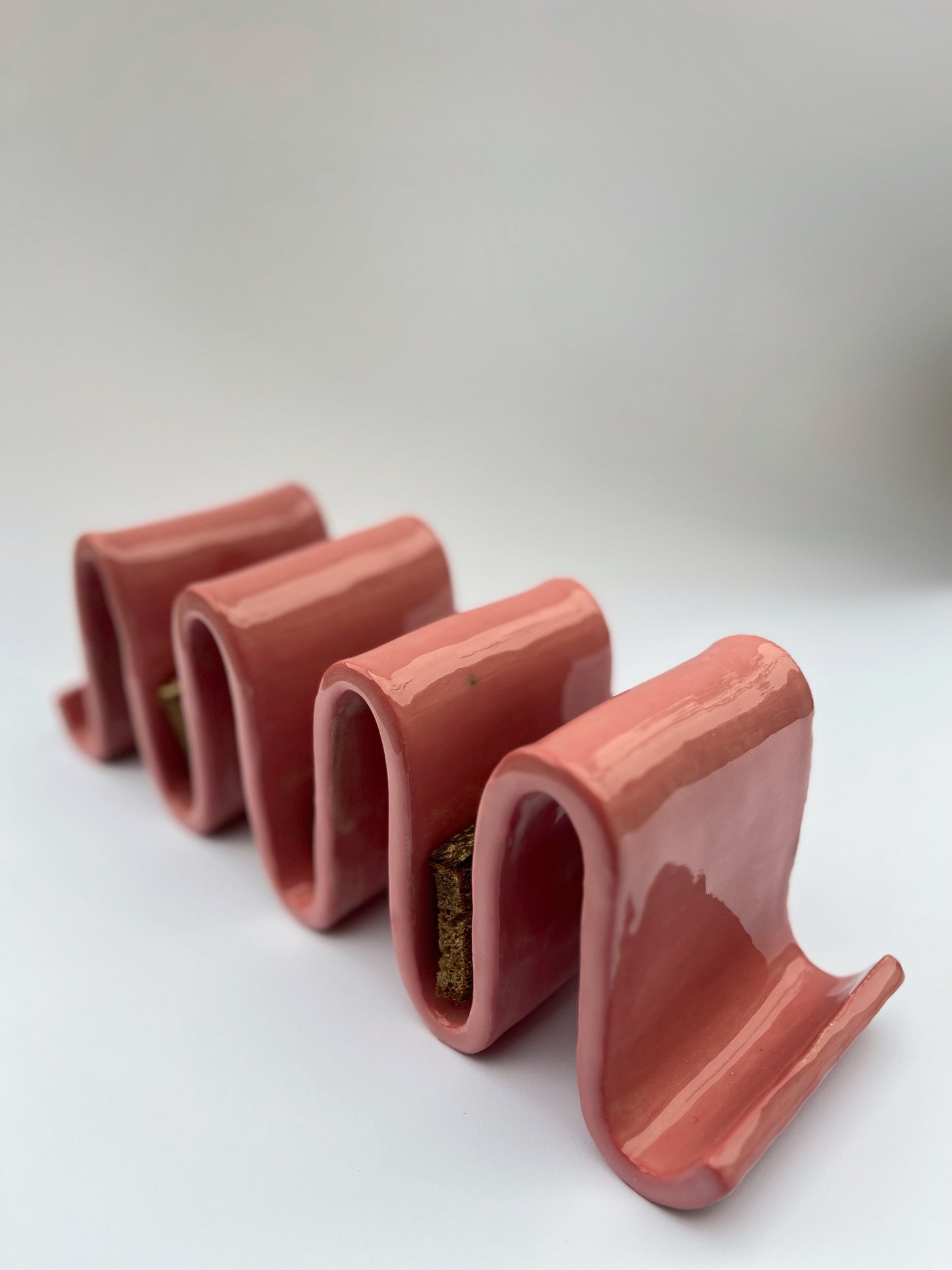 Porte-pain en grès blanc chamotté, engobe rose, en forme de vagues. Fait à la main à Paris par l'un de nos artisans. Doté de plusieurs usages, il pourrait tout à fait servir de porte-pain pour y déposer ses tartines grillées le matin, de porte livres sur un bureau ou une table de chevet, ou pour trier votre courrier dans votre entrée.