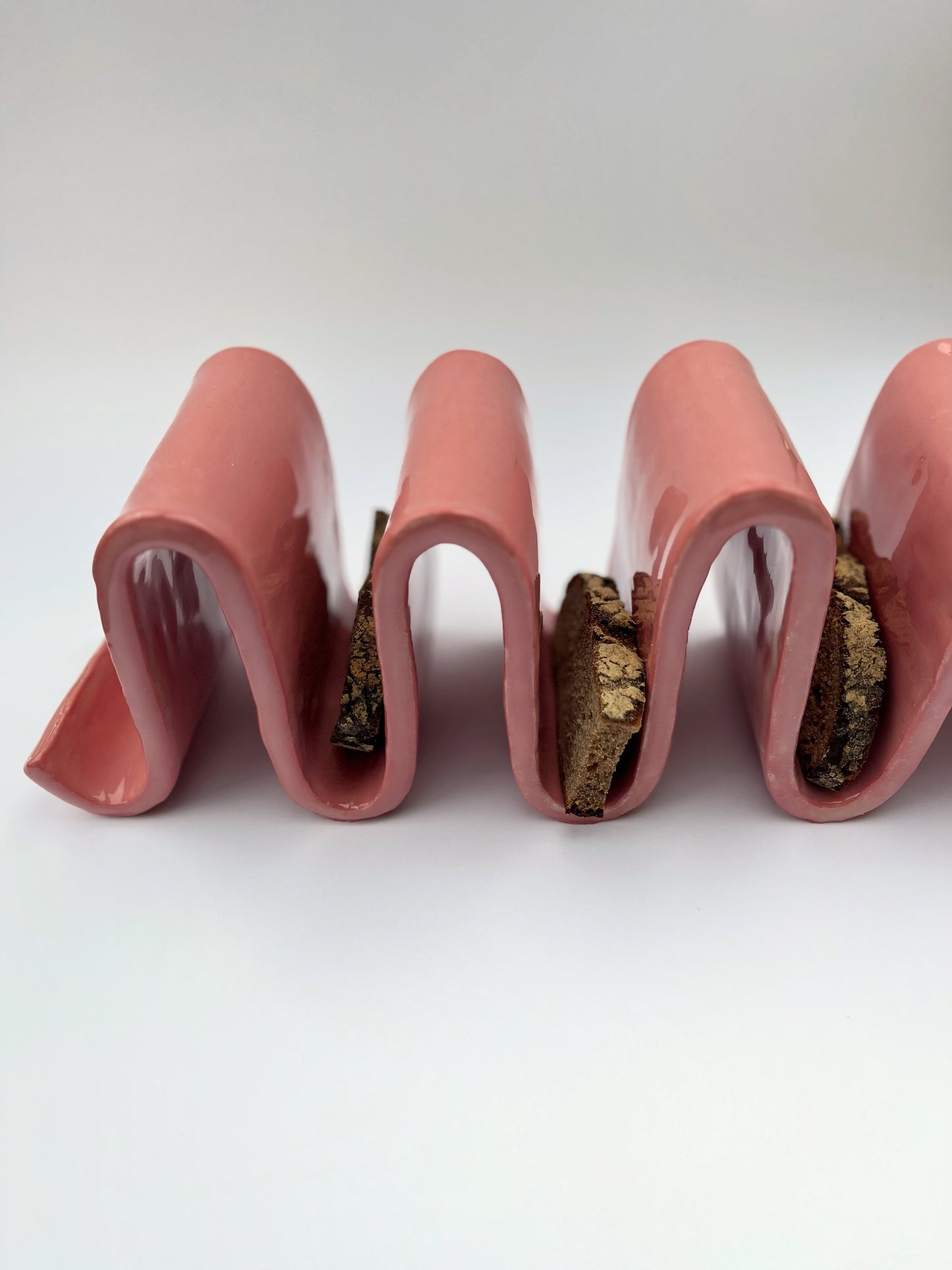 Porte-pain en grès blanc chamotté, engobe rose, en forme de vagues. Fait à la main à Paris par l'un de nos artisans. Doté de plusieurs usages, il pourrait tout à fait servir de porte-pain pour y déposer ses tartines grillées le matin, de porte livres sur un bureau ou une table de chevet, ou pour trier votre courrier dans votre entrée.