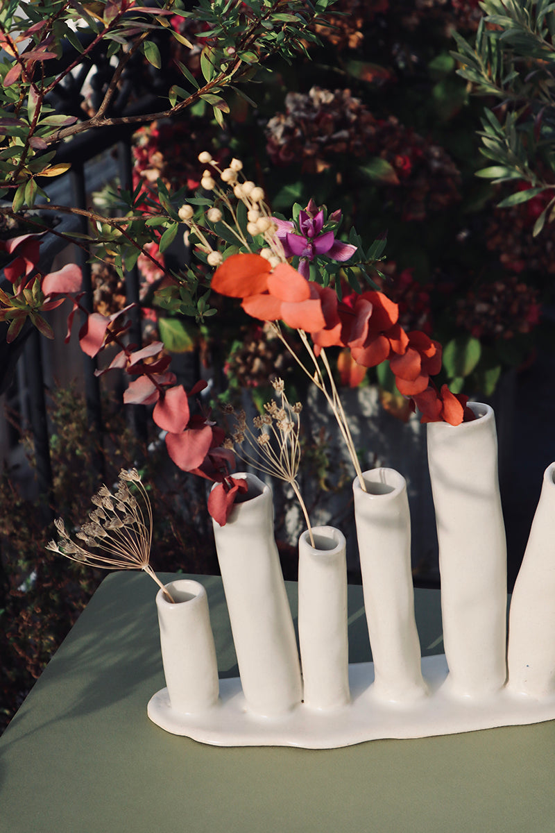 Soliflore en grès, fait à la main en région parisienne. Ikebana à six fleurs nous charme par son aspect délicat et original. Décliné en deux couleurs très minérales (vert et blanc), l'Ikebana saura habiller vos consoles, étagères, cheminées, ou même en centre de table. Ici soliflore blanc sur une table d'une terrasse. Email naturel.